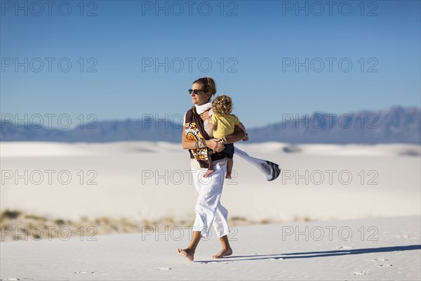Caucasian mother carrying son on sand dune