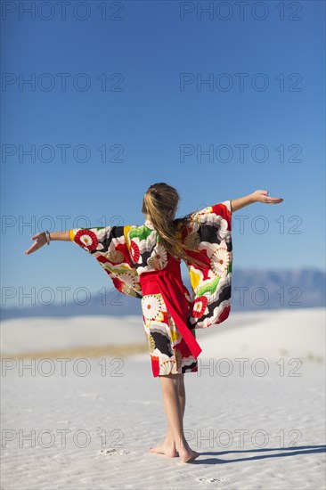 Caucasian girl with arms outstretched on sand dune