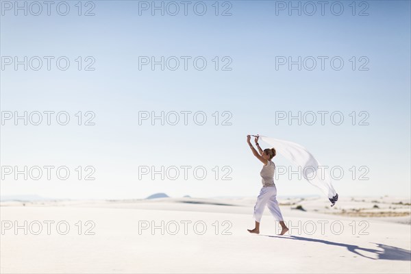 Caucasian woman playing with scarf on sand dune