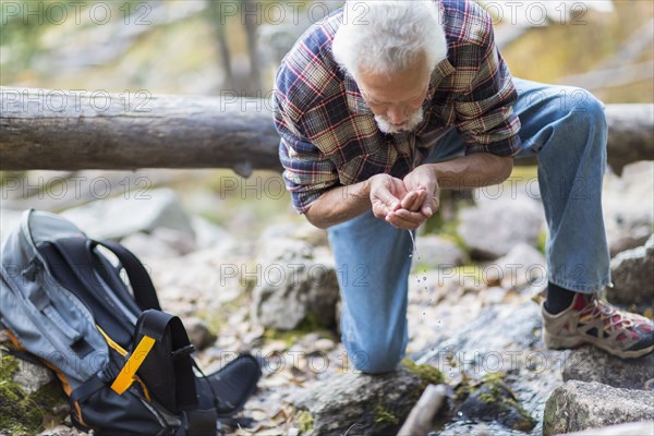 Caucasian hiker drinking water from creek in forest