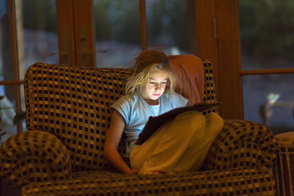 Caucasian girl using digital tablet in armchair at night
