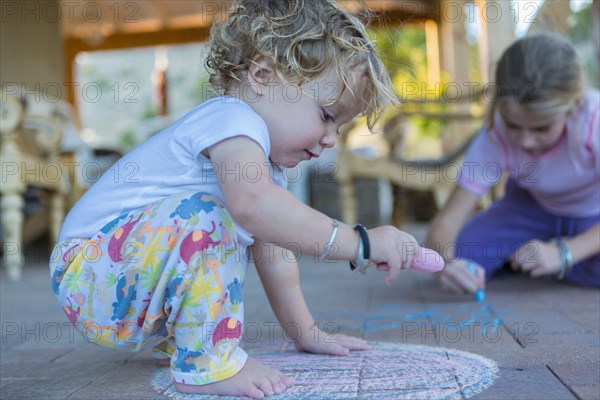 Caucasian children drawing with chalk on patio