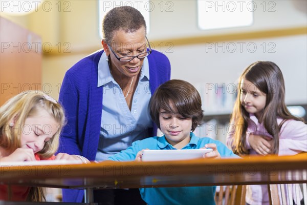 Teacher helping student use digital tablet in library