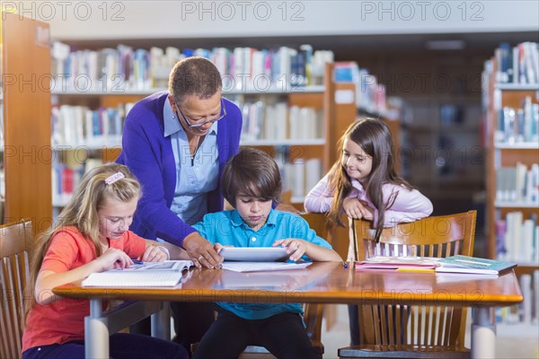 Teacher helping student use digital tablet in library