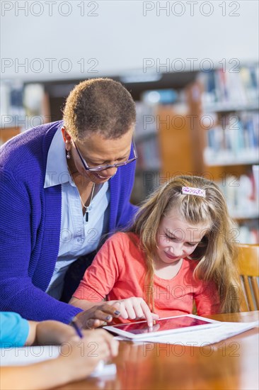 Teacher helping student use digital tablet in library