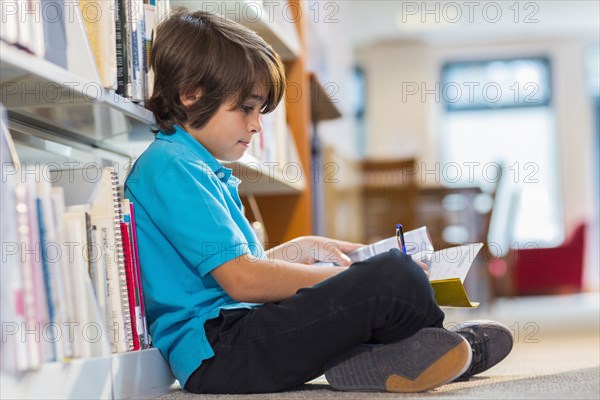 Mixed race student writing in notepad on floor in library