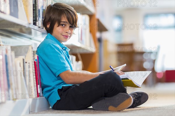 Mixed race student writing in notepad on floor in library