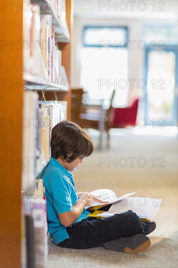 Mixed race student reading books on floor in library