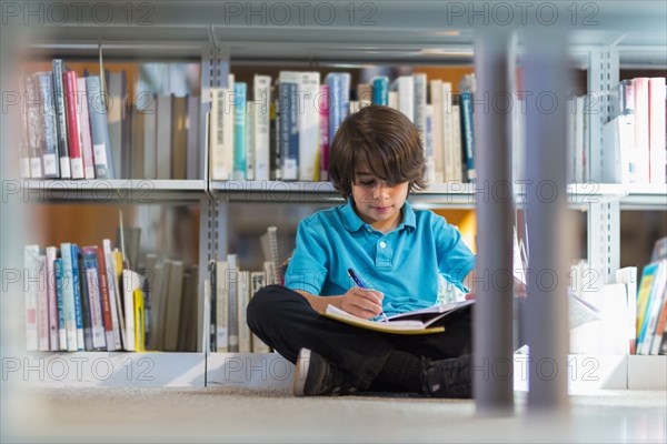 Mixed race student writing in notebook on floor in library