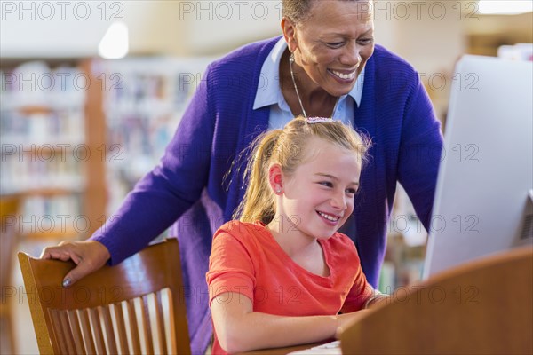 Teacher helping student use computer in library