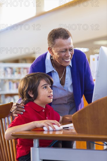 Teacher helping student use computer in library