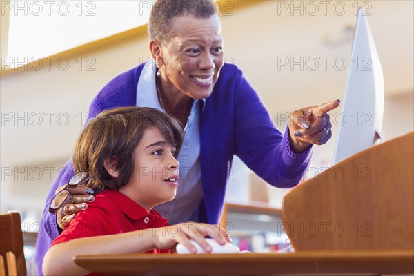 Teacher helping student use computer in library