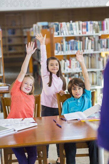 Students raising their hands in library