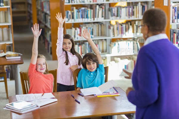 Students raising their hands in library