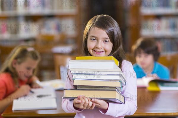 Student carrying stack of books in library