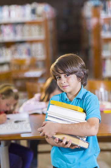 Student carrying stack of books in library