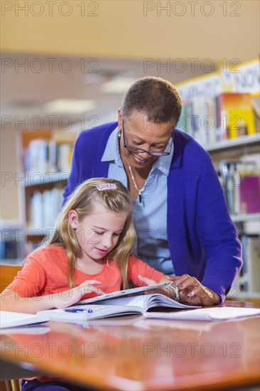 Teacher helping student use digital tablet in library