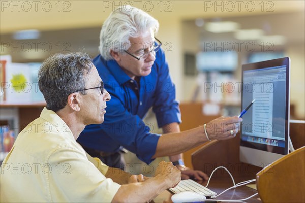 Teacher helping adult student use computer in library