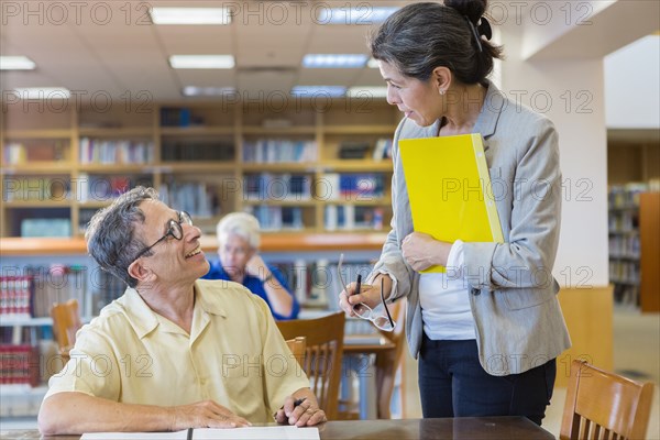 Teacher helping adult student in library