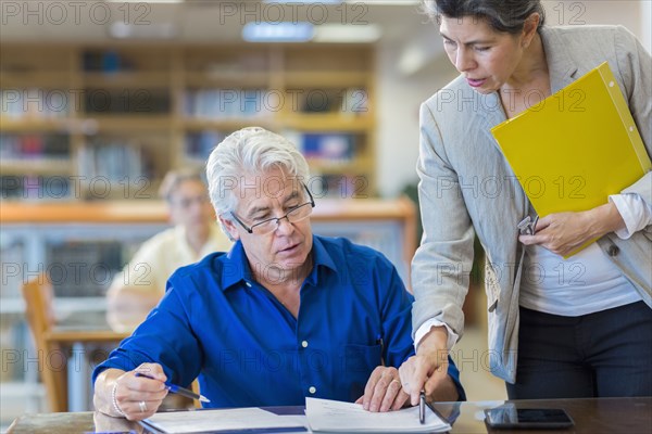 Teacher helping adult student in library