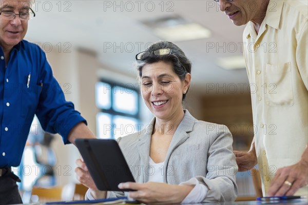Teacher helping adult students use digital tablet in library