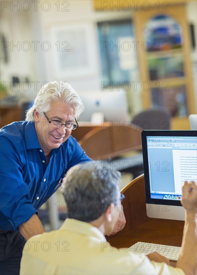 Teacher helping adult student use computer in library