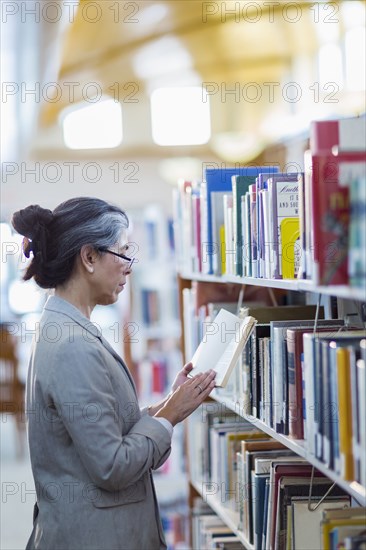 Older Hispanic woman reading book in library
