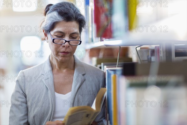 Older Hispanic woman reading book in library