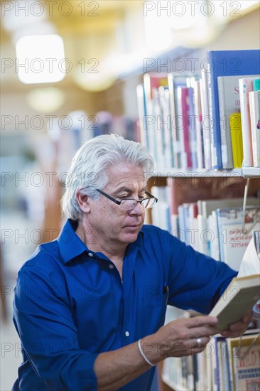 Older Hispanic man reading book in library