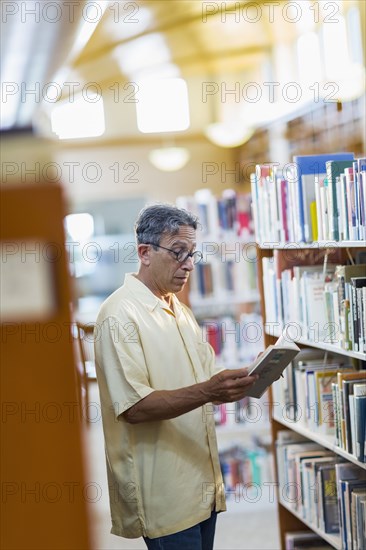 Older Caucasian man reading book in library