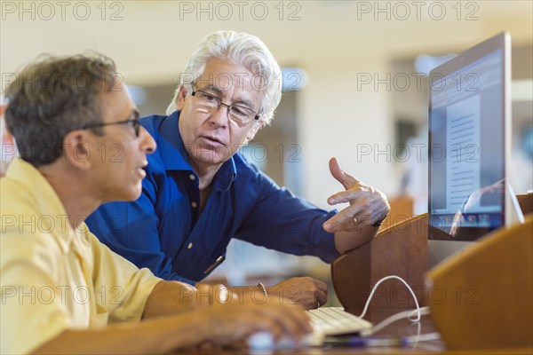 Teacher helping adult student use computer in library