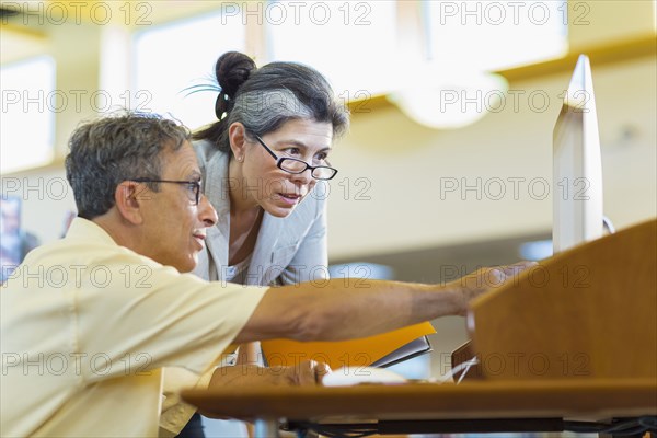 Teacher helping adult student use computer in library