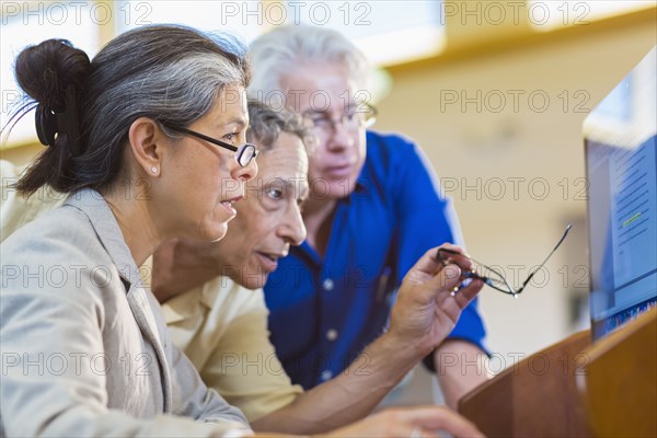 Teacher helping adult students use computer in library