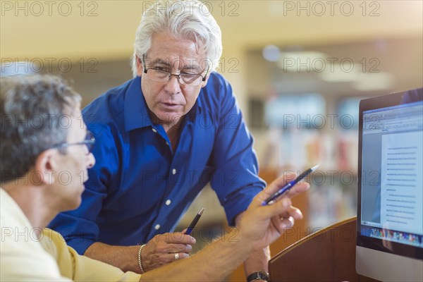 Teacher helping adult student use computer in library