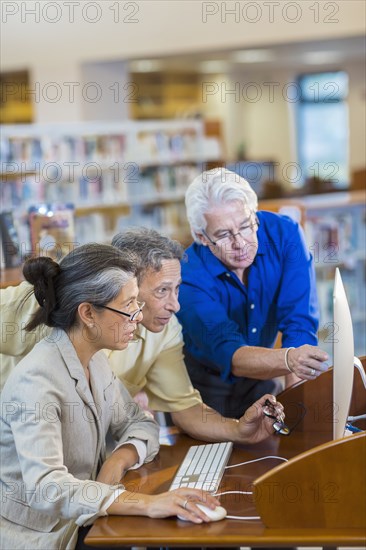 Teacher helping adult students use computer in library