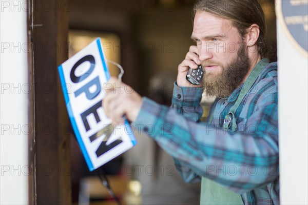 Caucasian server on telephone hanging open sign on cafe window