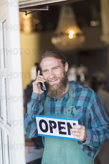 Caucasian server on telephone hanging open sign on cafe window