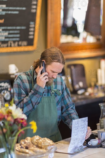 Caucasian server on telephone reading clipboard in cafe