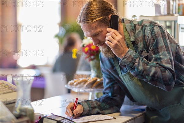 Caucasian server on telephone writing on clipboard