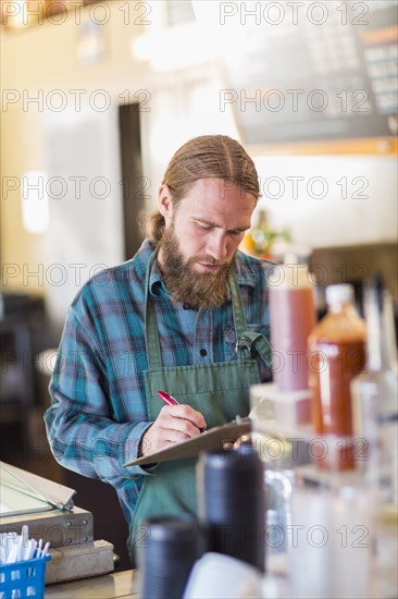 Caucasian server writing on clipboard in cafe