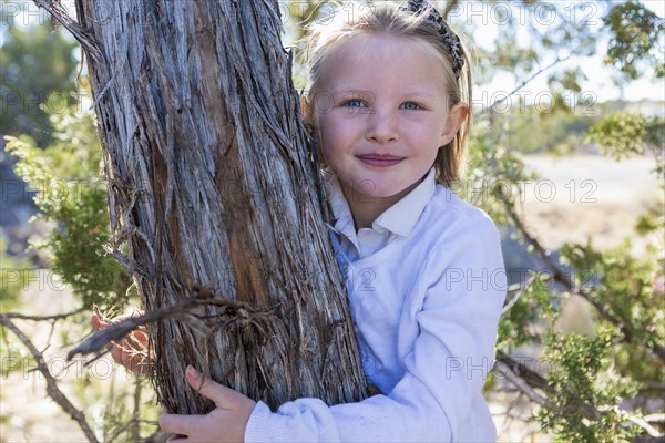 Smiling girl hugging tree