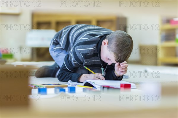 Caucasian boy writing in notebook on floor in classroom