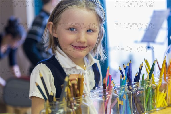 Mixed race girl smiling near multicolor pencils in classroom