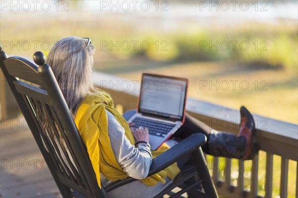 Older Caucasian woman using laptop on porch