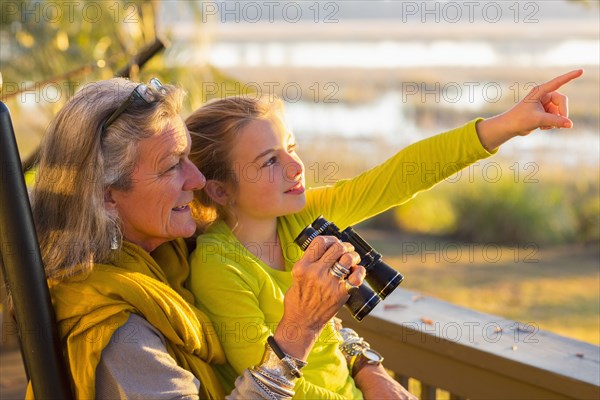 Caucasian grandmother and granddaughter using binoculars on porch