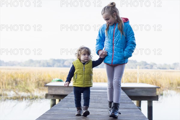Caucasian brother and sister walking on wooden dock