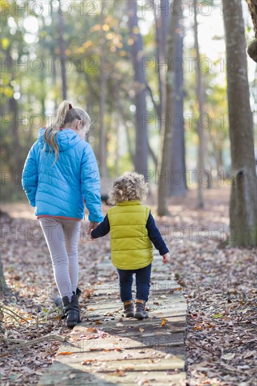 Caucasian brother and sister walking on wooden walkway