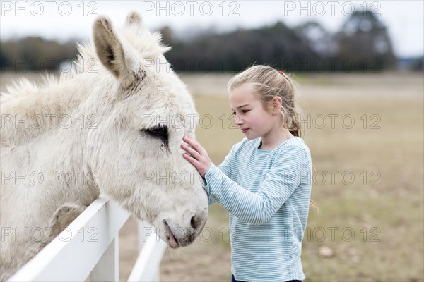 Caucasian girl petting donkey in field