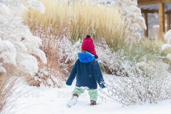 Caucasian baby boy walking in snowy garden