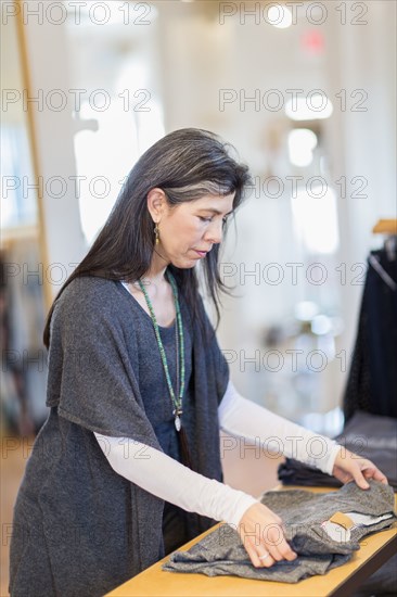 Hispanic small business owner folding clothes in store
